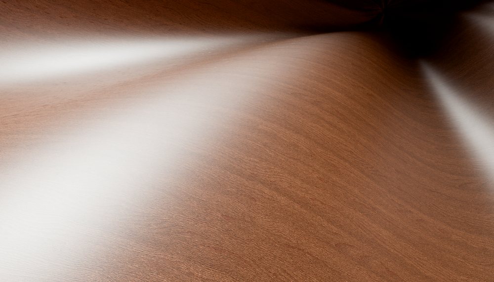 Close-up of a polished wooden surface with light reflections showing natural wood grain texture.