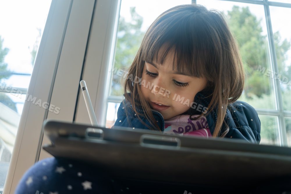 Young white girl using a digital tablet indoors near a window