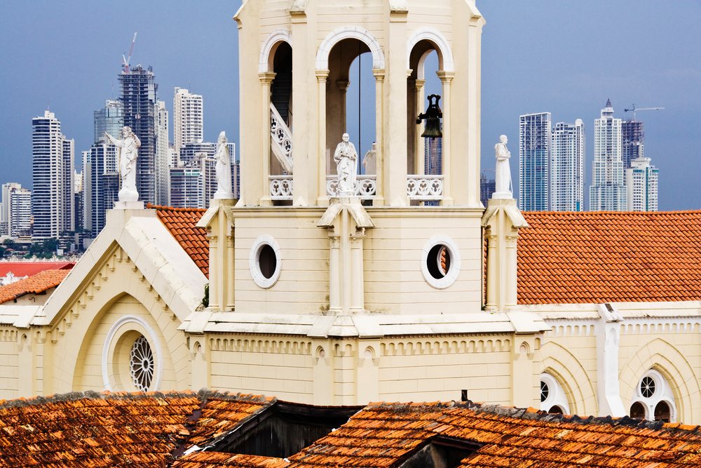 Bell tower of Iglesia de San Francisco with Panama City skyline and modern skyscrapers under a cloudy sky.