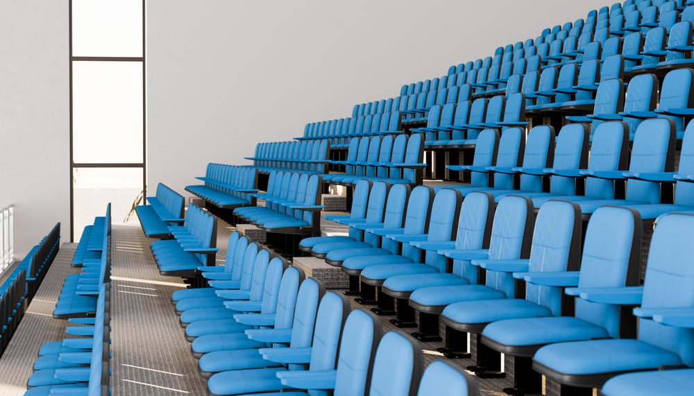 Blue upholstered seats with armrests arranged in tiered rows inside a modern indoor auditorium conference room.