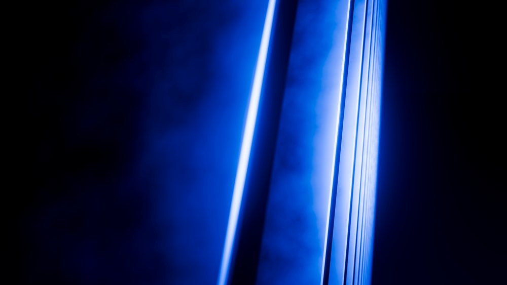 Blue neon light beams form abstract vertical glowing stripes against a dark background.