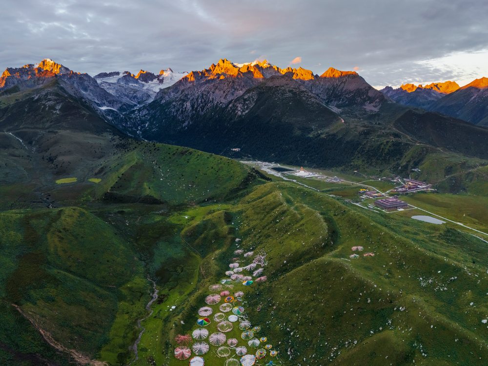 Zhuqing Wujian Zen Forest Monastery on a grassy hillside with colorful tents and rocky mountain peaks, Sichuan Province, People's Republic of China.
