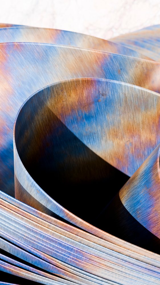 Curved metal sheets featuring colorful rust-like patterns creating an abstract industrial texture and pattern.