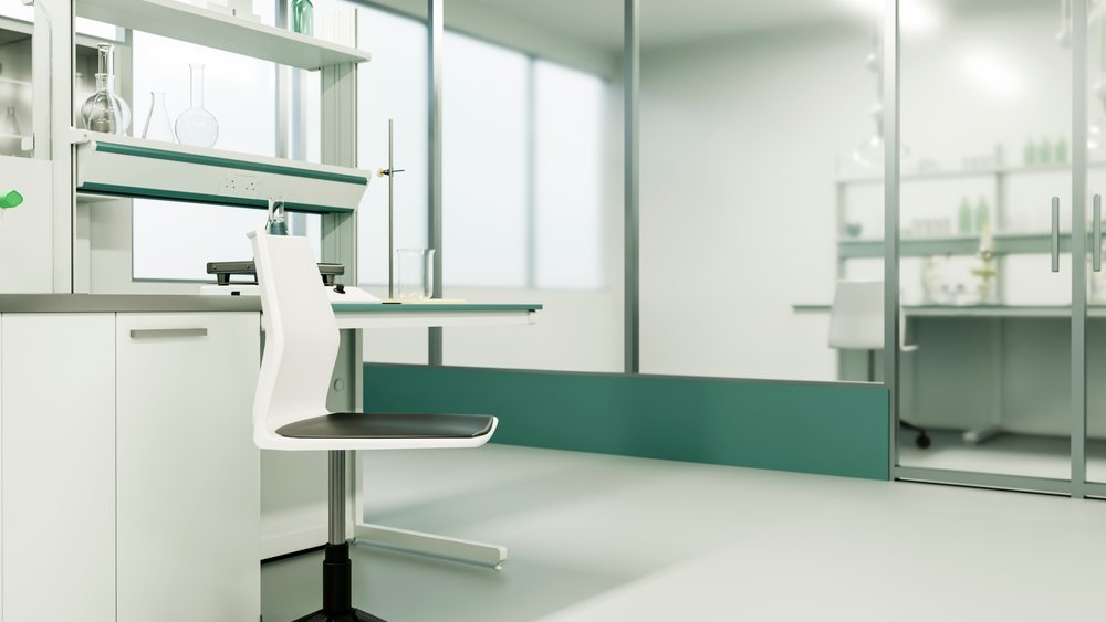 Laboratory chair with black seat and glass beaker and flasks on a white bench in a modern sterile research lab with metal shelving and glass wall.