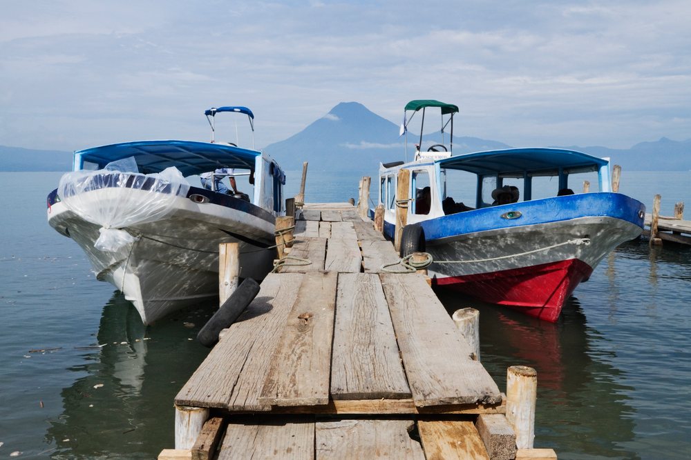 Two water taxis docked at a wooden pier on Lake Atitlan with a volcanic mountain in the background, Solola Department, Guatemala.