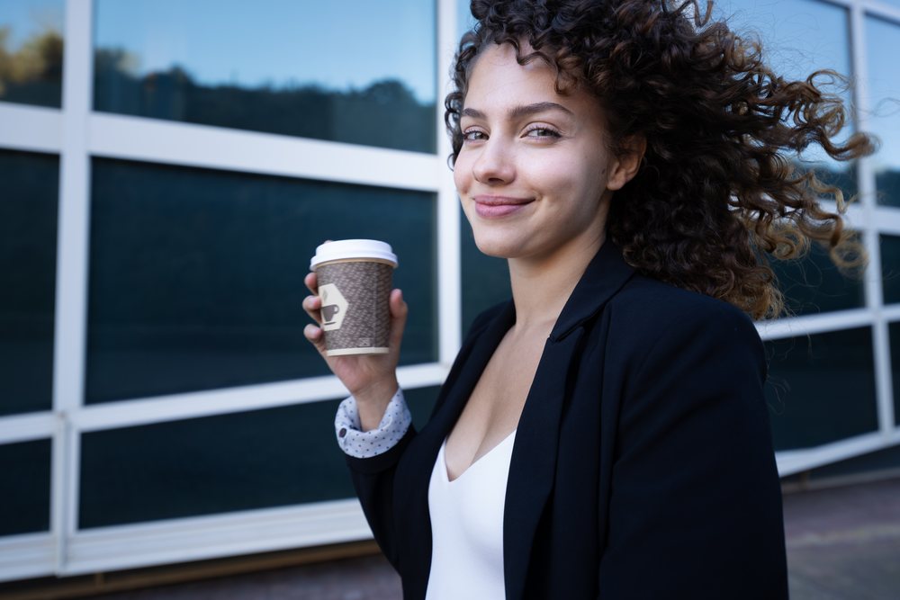 Woman holding a coffee cup and smiling outdoors, businesswoman, business trip, Spain, Santiago De Compostela.