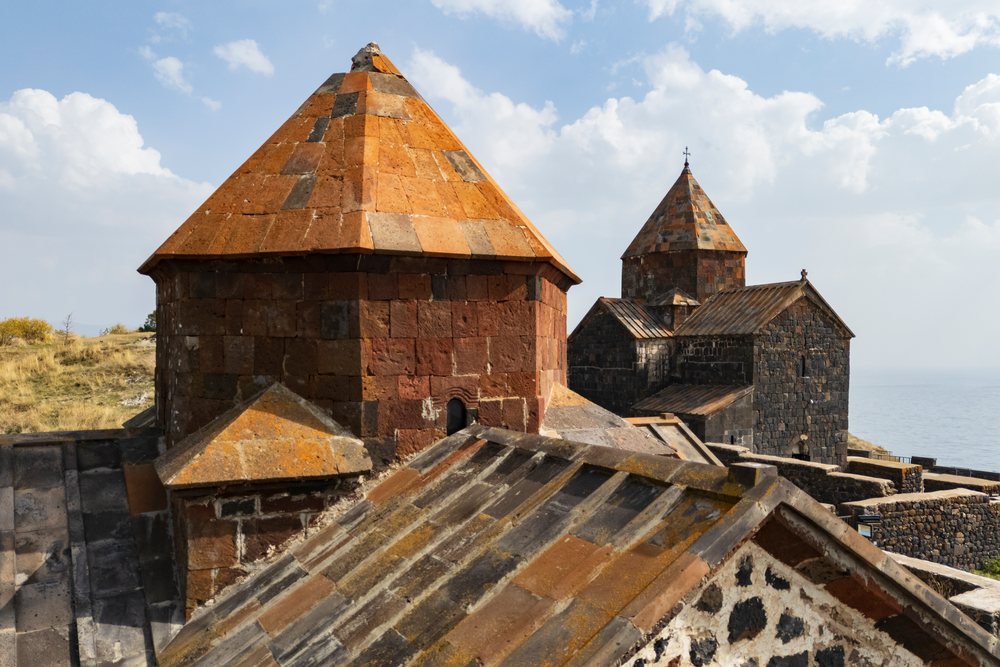 Sevanavank Monastery with orange tiled roofs and stone walls beside Lake Sevan on a partly cloudy day, Gegharkunik Province, Armenia.