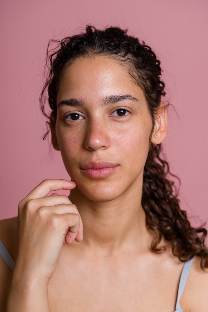 Studio portrait of a young woman with curly brown hair and freckles against a pink background, beauty shoot, Spain.