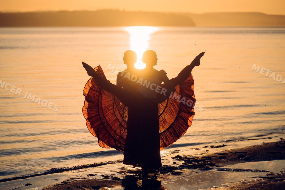 Two white women performing partner acrobatics on a beach at sunset