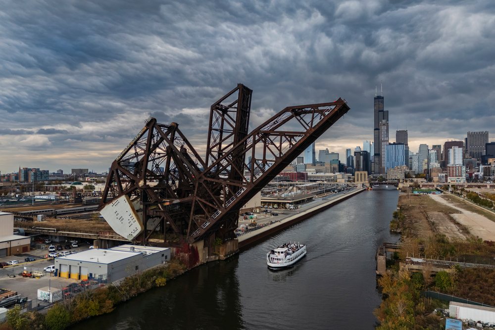 Steel Cantilever Bridge raised over the Chicago River with a boat passing beneath and the city skyline behind under a cloudy sky, Americana, Historic, Illinois, USA.