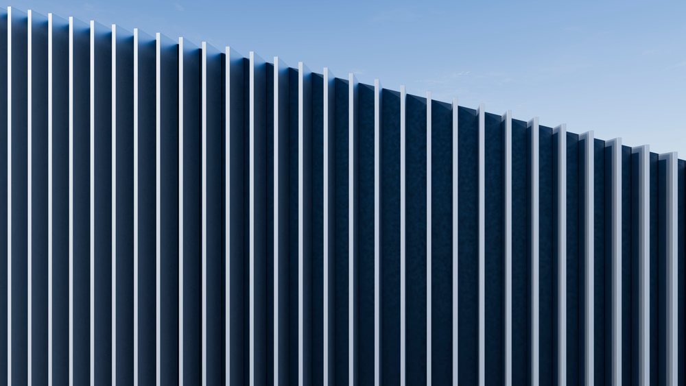 Modern building facade with vertical fins casting shadows under blue sky in urban setting.