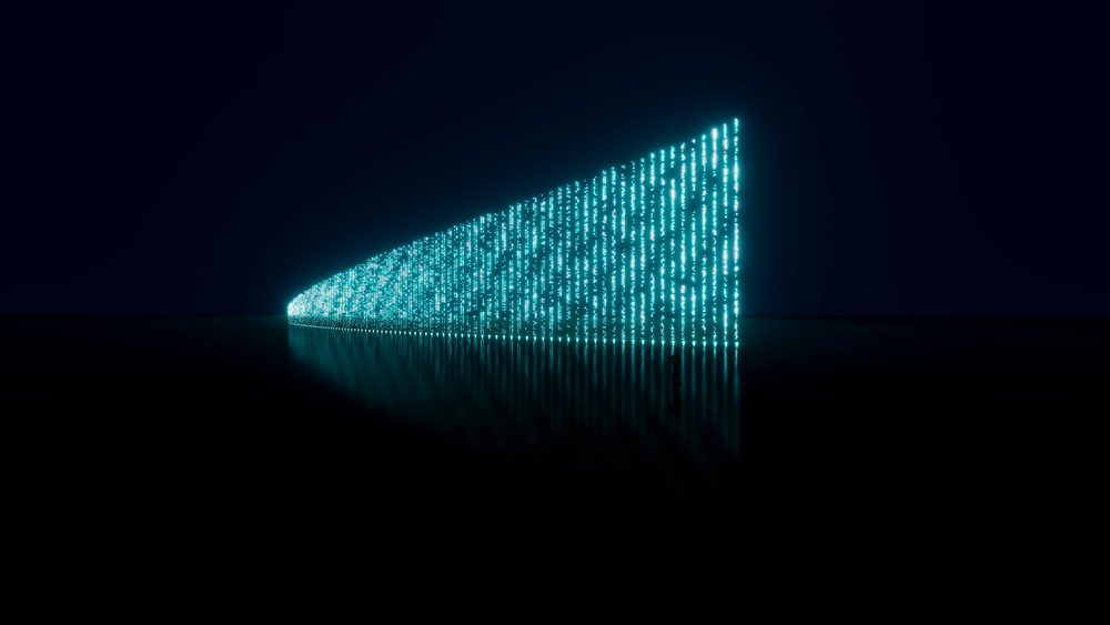Human silhouette stands near a vertical glowing digital data wall with blue matrix-style code reflected on a dark surface in a futuristic setting.