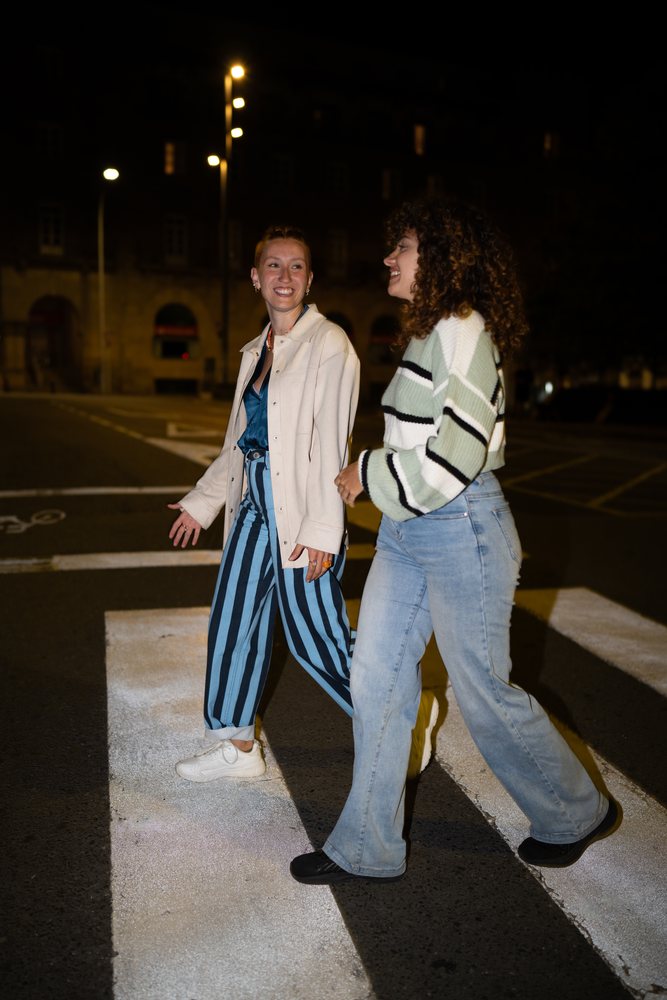 Two women walking and smiling on a crosswalk at night, friendship, Santiago De Compostela, Spain.