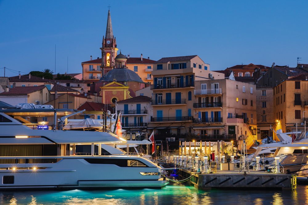 Harbour at Calvi at Dawn with yachts docked and historic buildings reflecting in the water under a clear sky, Travel Photography, Corsica, France.