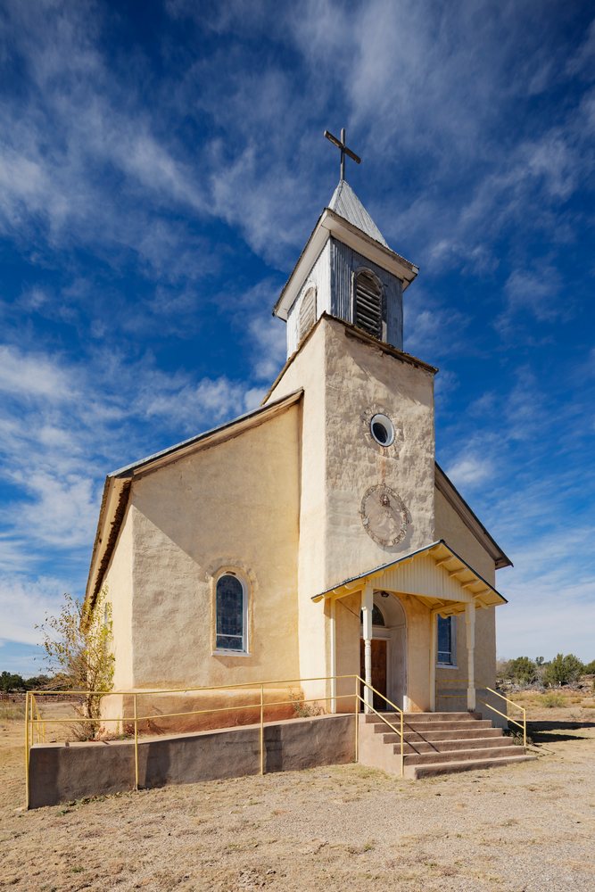 Sacred Heart Church building with stucco exterior and bell tower topped with cross under blue sky, Americana, Historic, Dilia, New Mexico, USA.