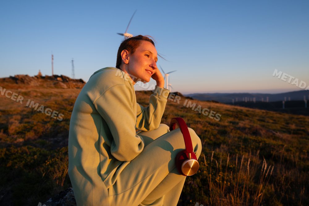A white woman enjoys a peaceful sunset with wind turbines in Galicia