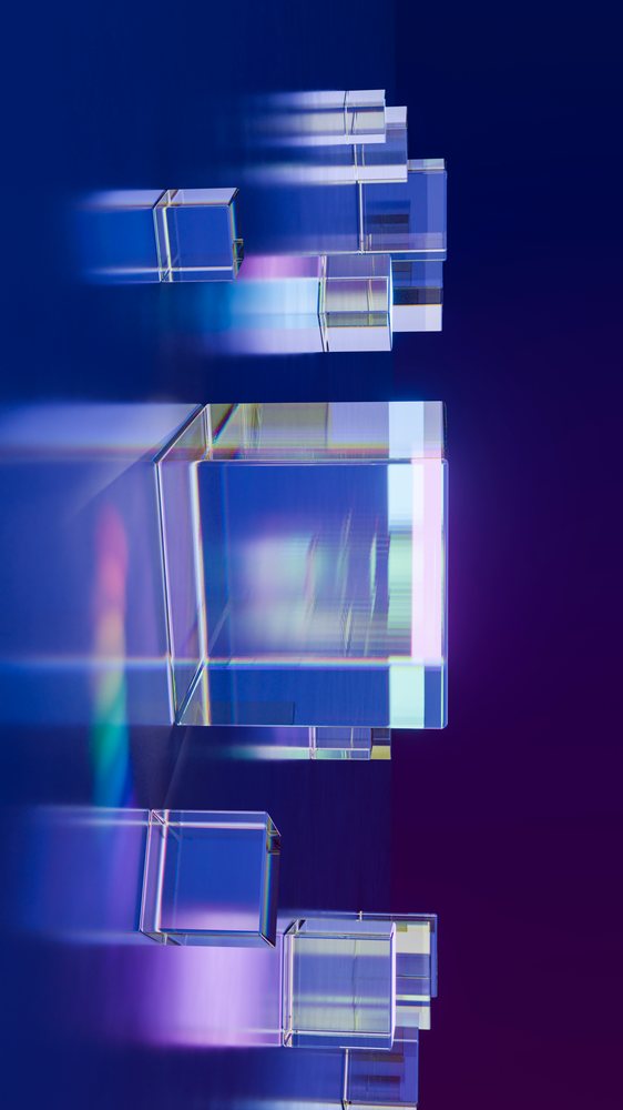 Multiple transparent glass cubes on a reflective surface with colorful prism light reflections against a blue and purple background.