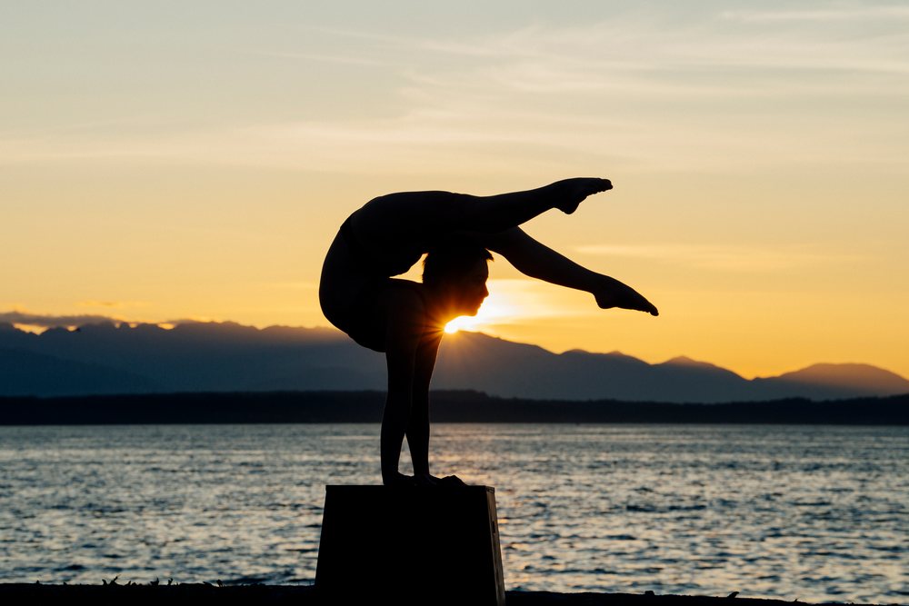Silhouette of a person performing a yoga handstand at sunset by a mountain lake on a rectangular platform, USA.