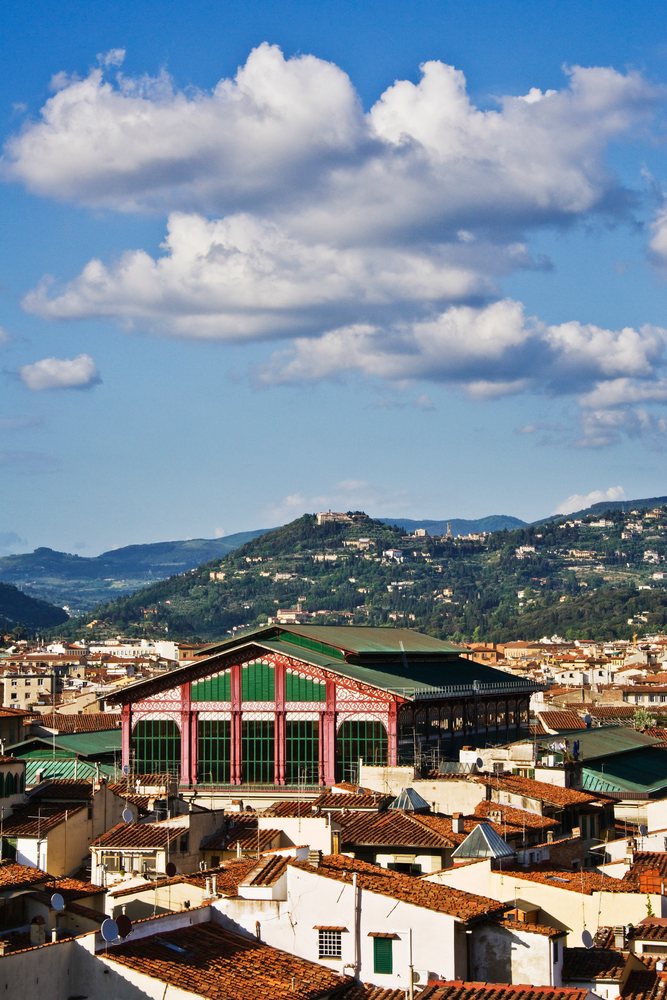 Mercato Centrale market building and Florence rooftops with green hills and clouds in the background, Italy.