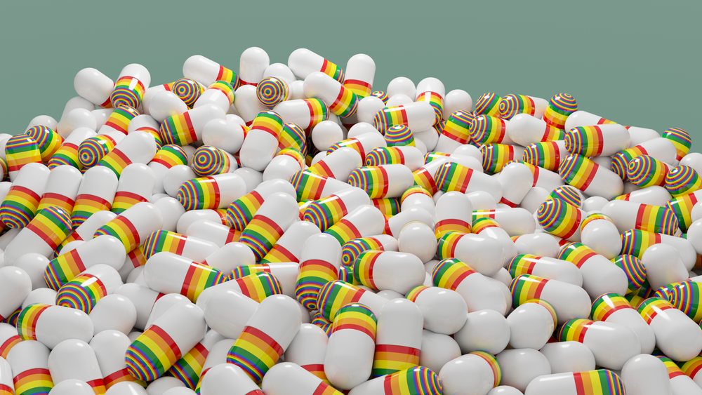 Pile of white medicine capsules with rainbow-colored bands against a green background.