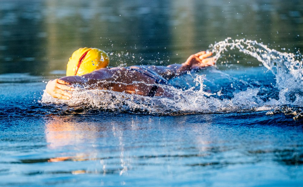 Swimmer performing backstroke in open water with splashing water, USA.