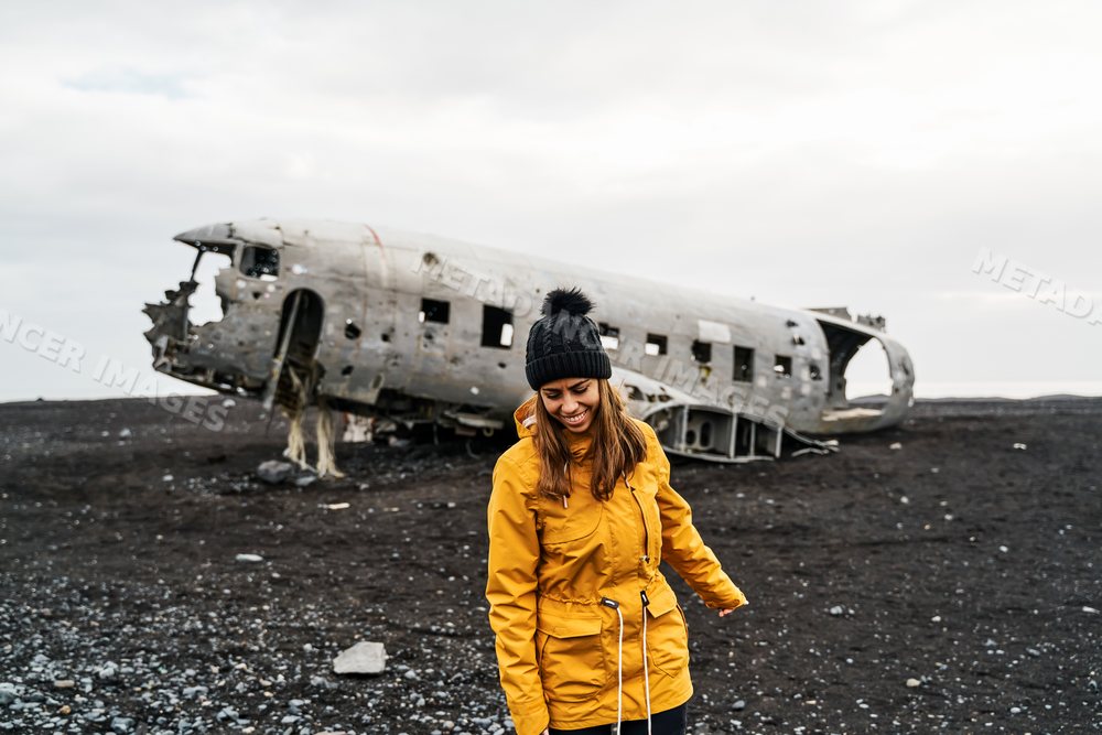A white woman smiles in front of an abandoned airplane wreck