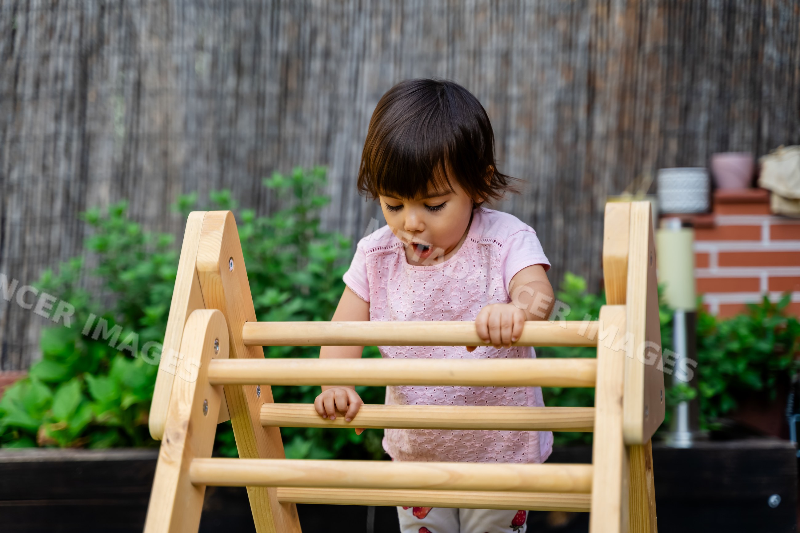 Toddler white girl playing on wooden climbing frame outdoors