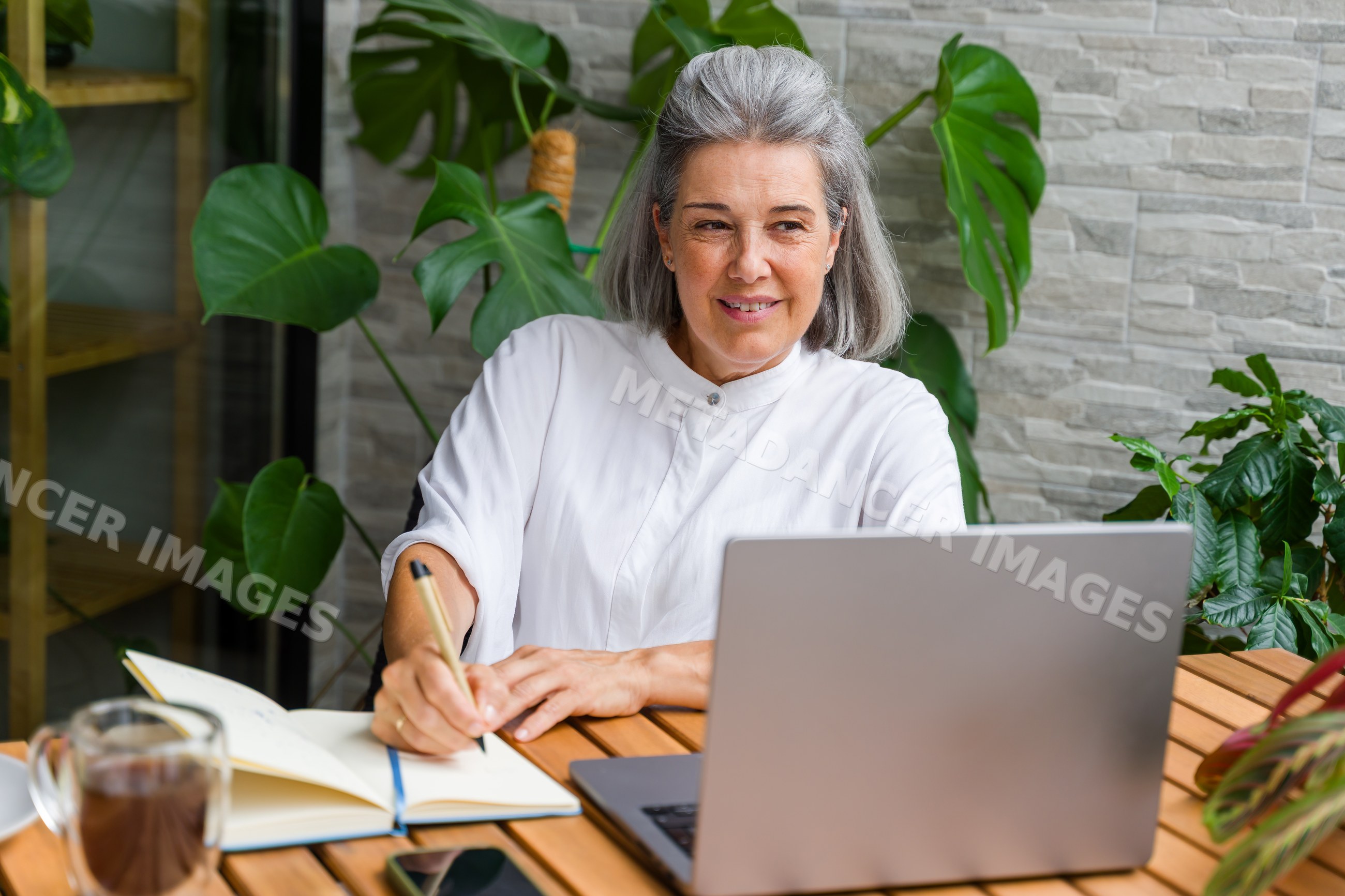 White Woman writing in notebook using laptop at wooden table
