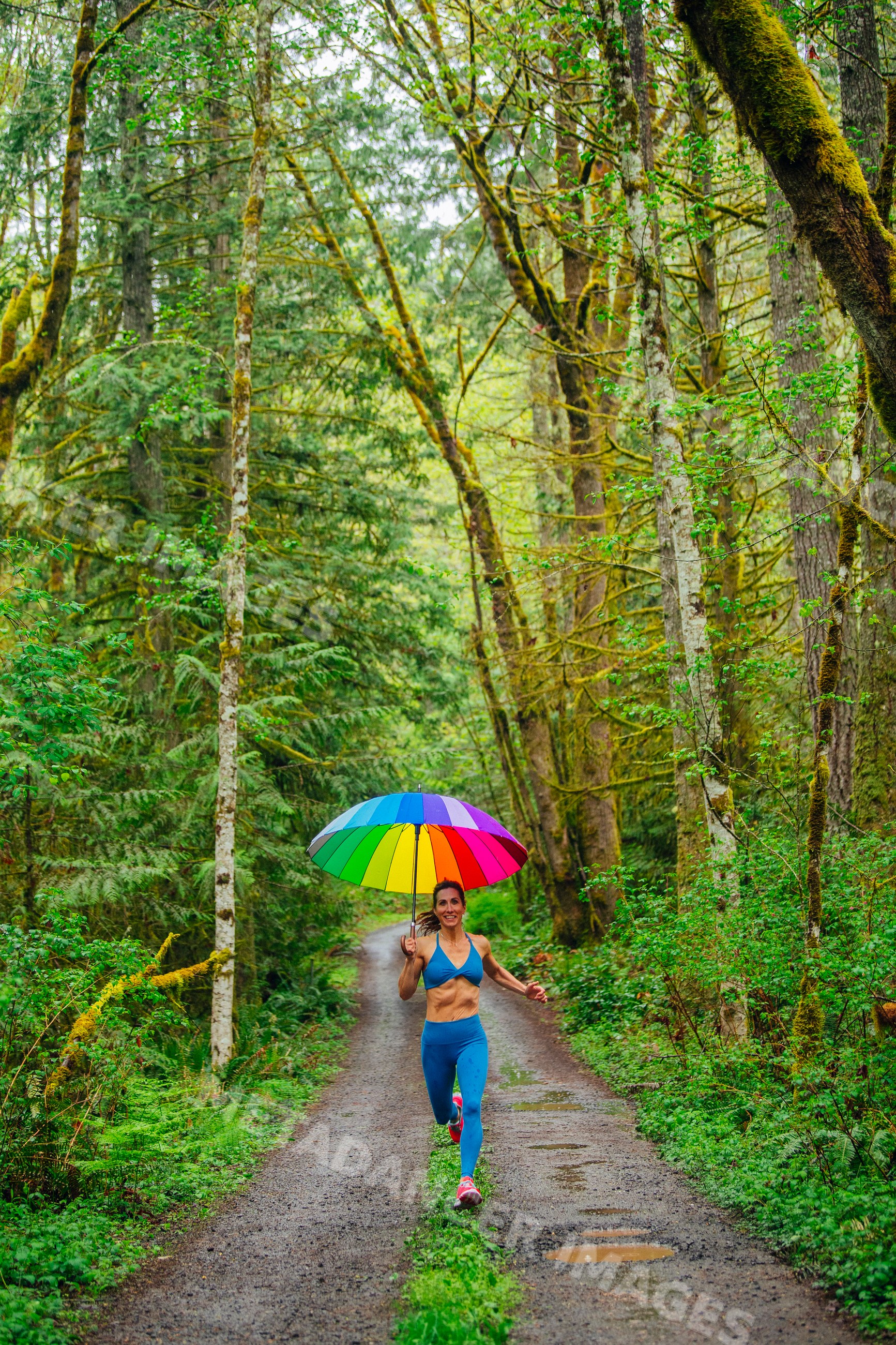 White woman running on forest trail holding rainbow umbrella