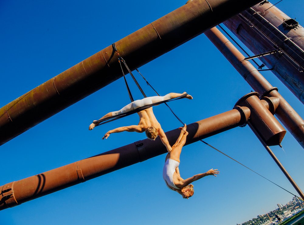 Two acrobats performing aerial straps routine outdoors with industrial