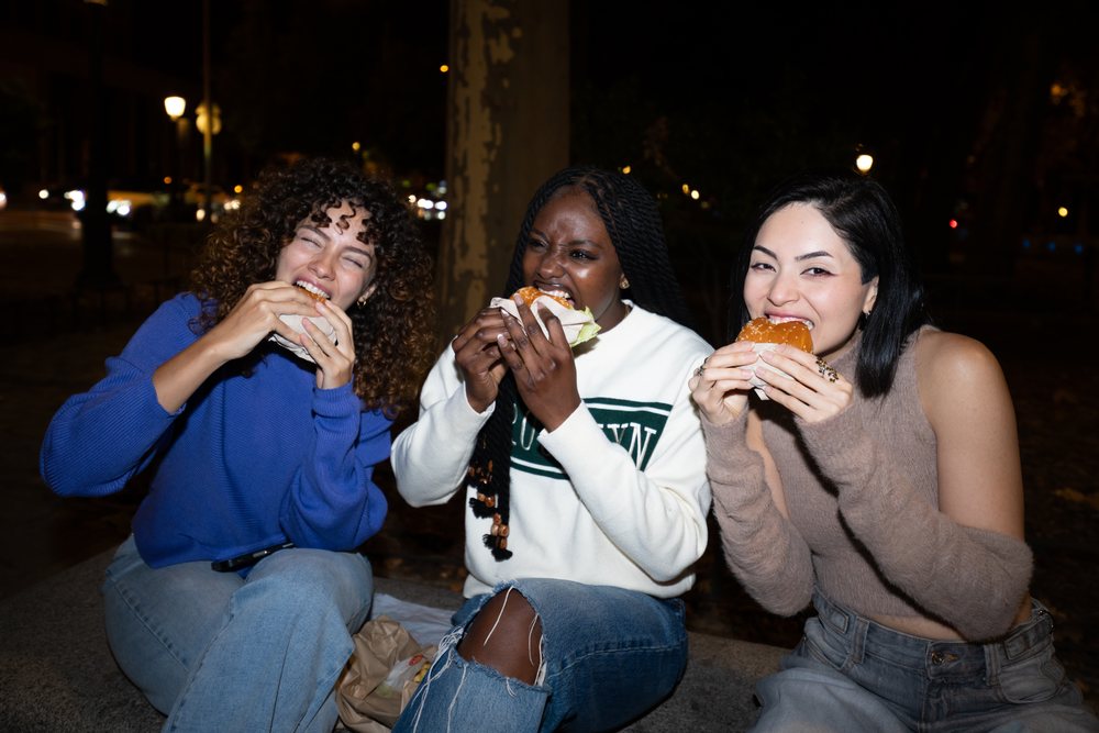 Friends eating burgers outdoors at night in urban street setting