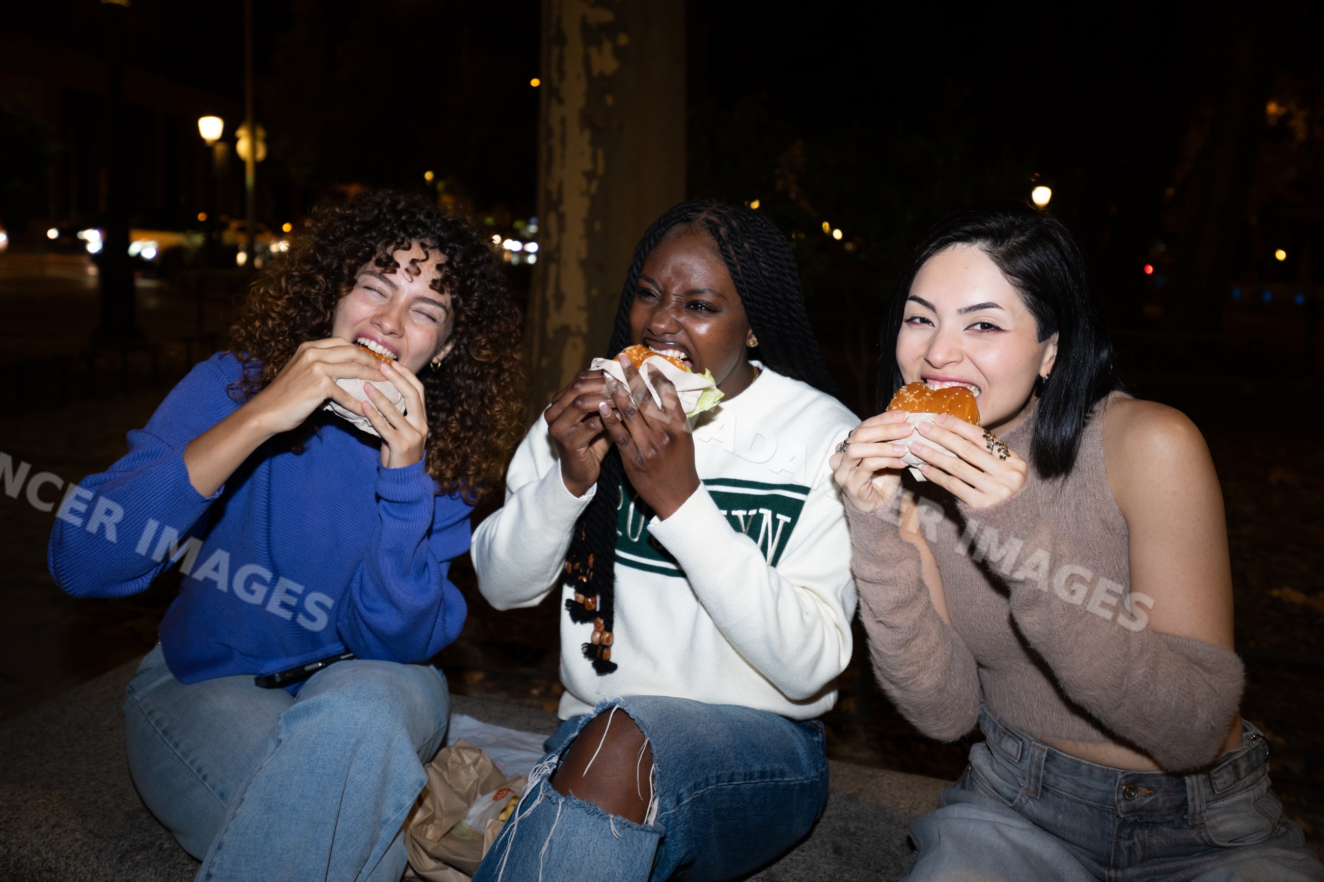 Friends eating burgers outdoors at night in urban street setting