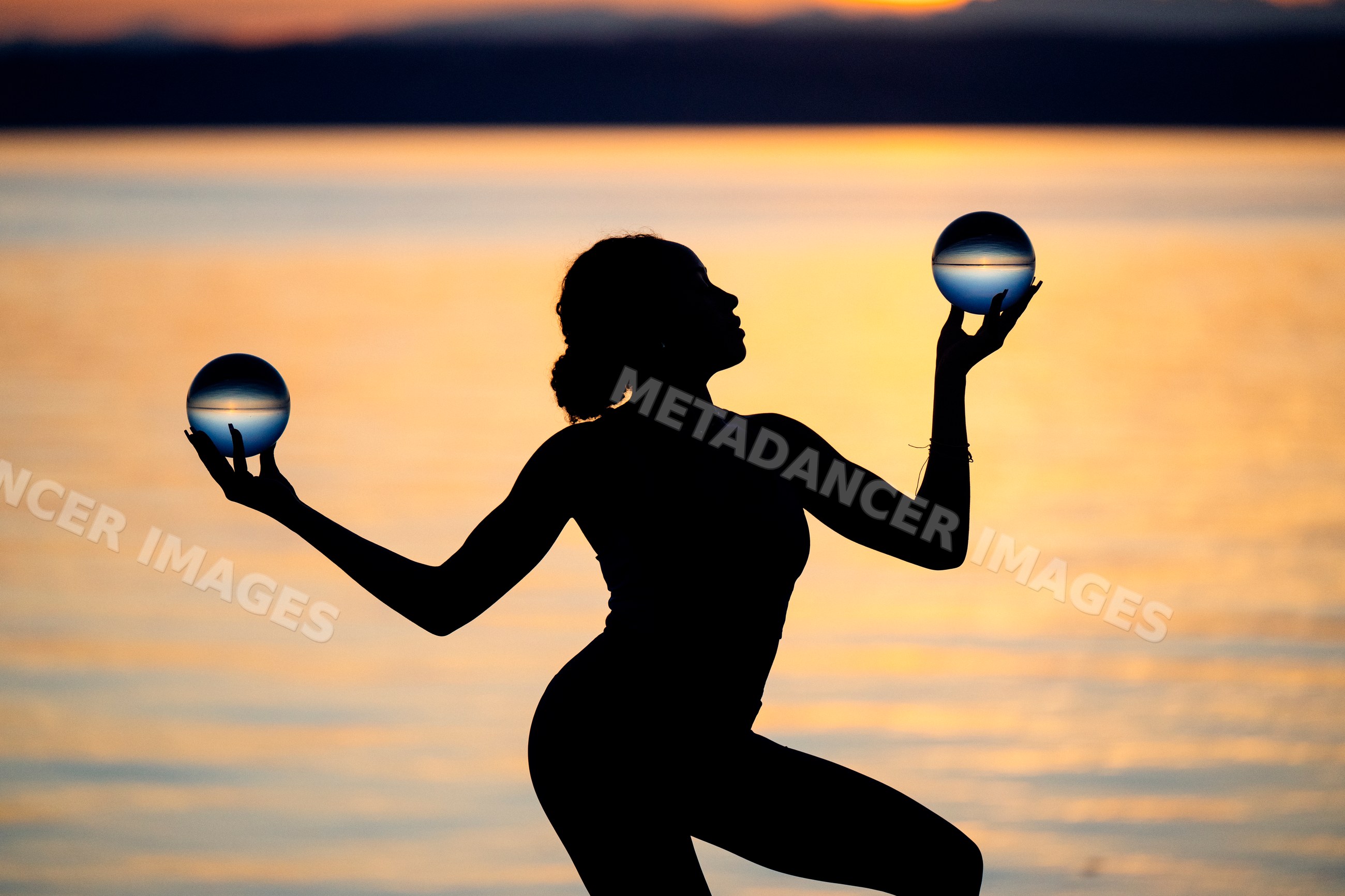Hispanic woman in silhouette balancing crystal balls at sunset