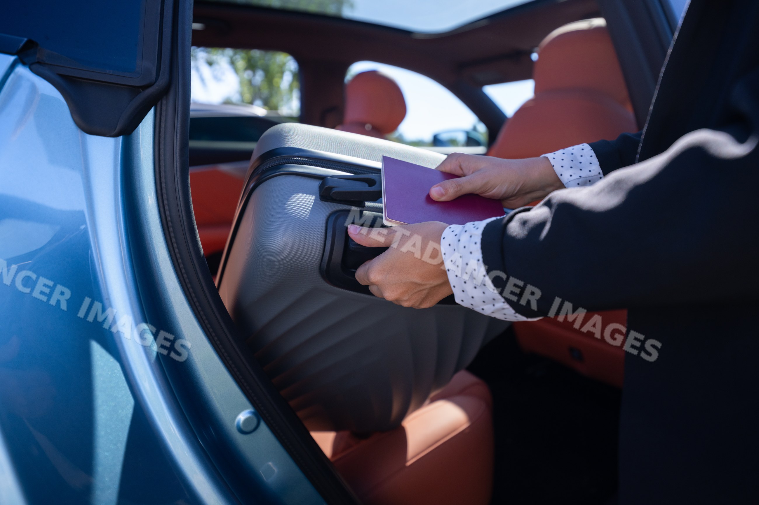 Businesswoman loading suitcase into car with passport during travel