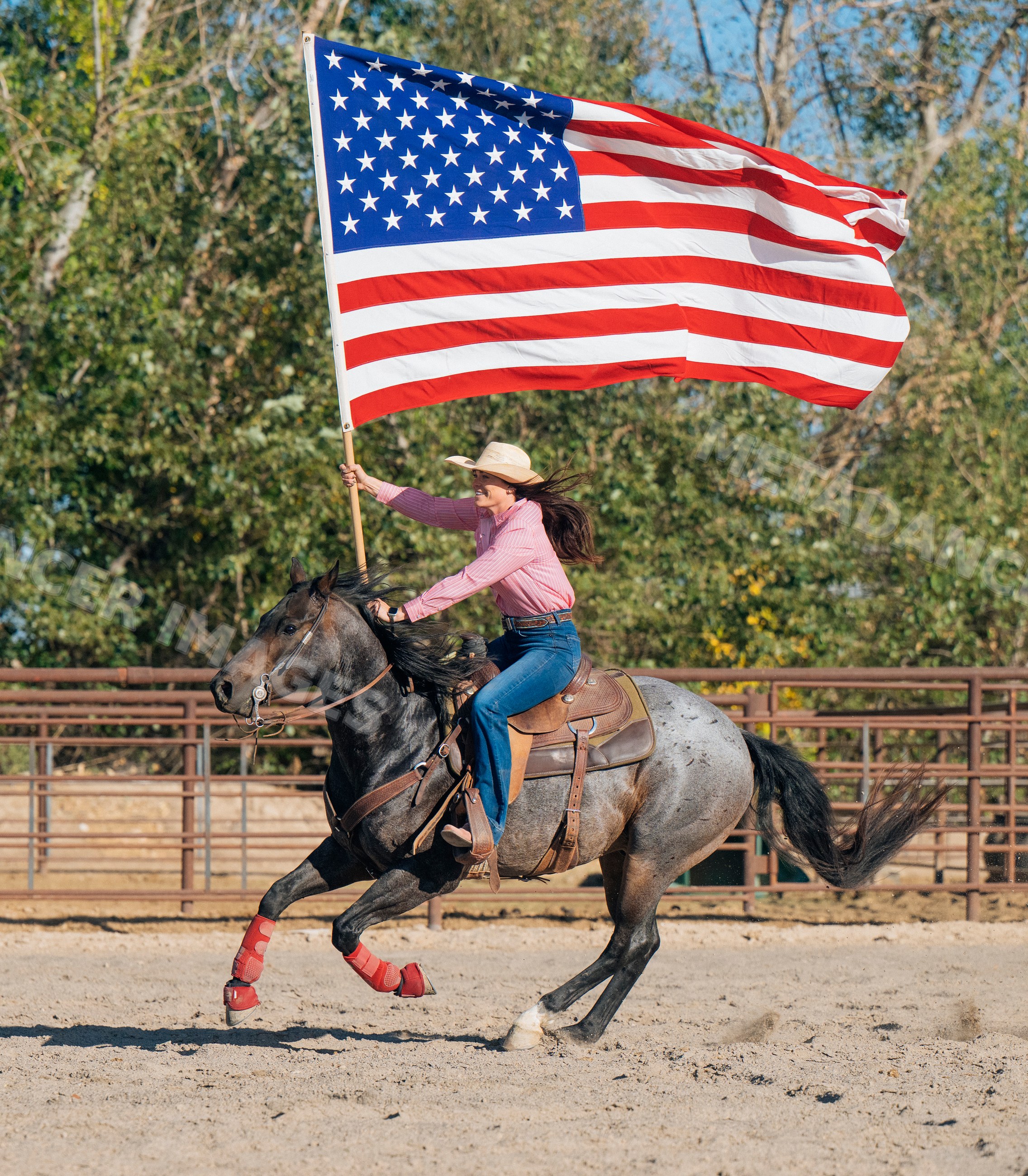 White woman riding horse in arena carrying large american flag