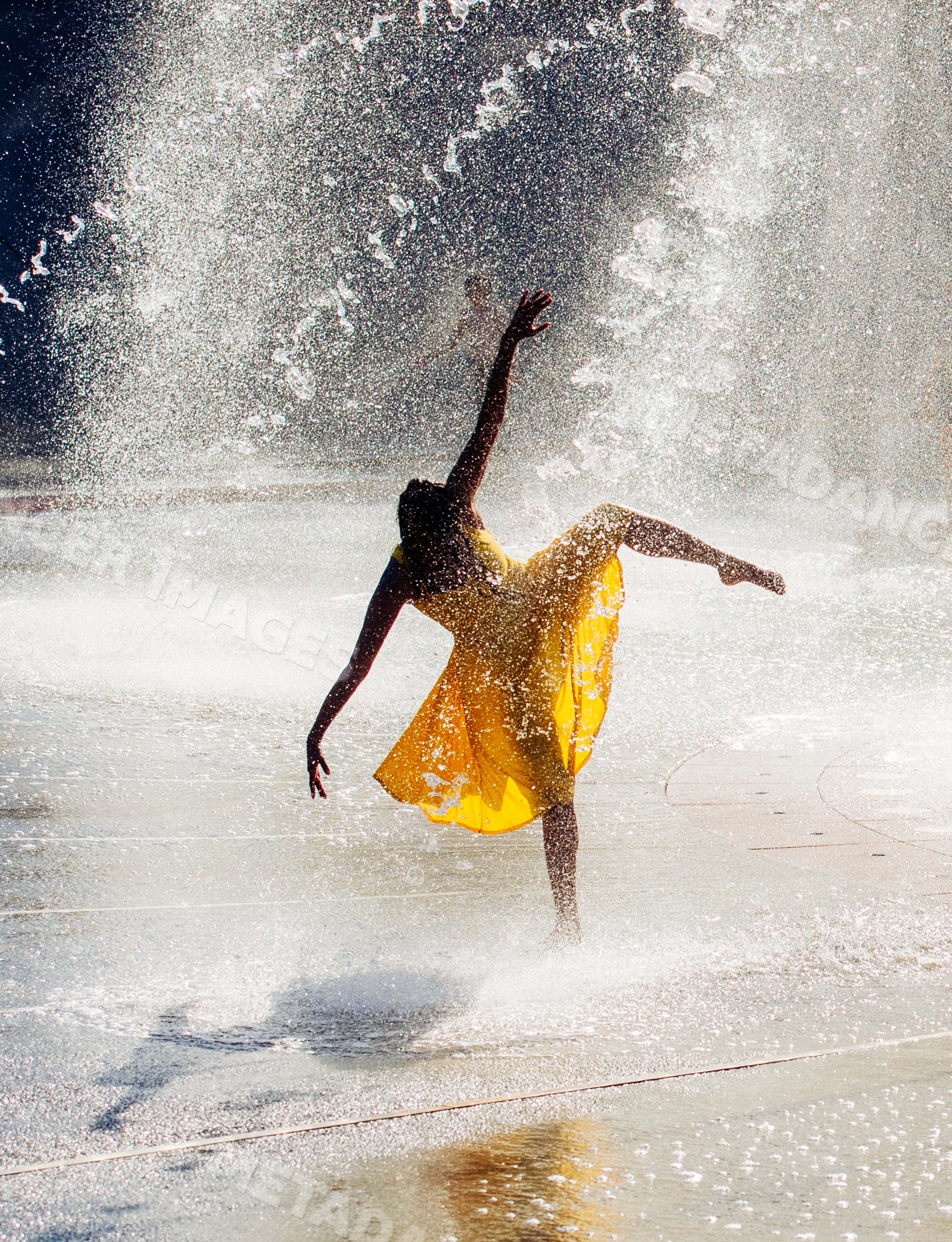 South Asian dancer in yellow dress performs graceful pose amid water