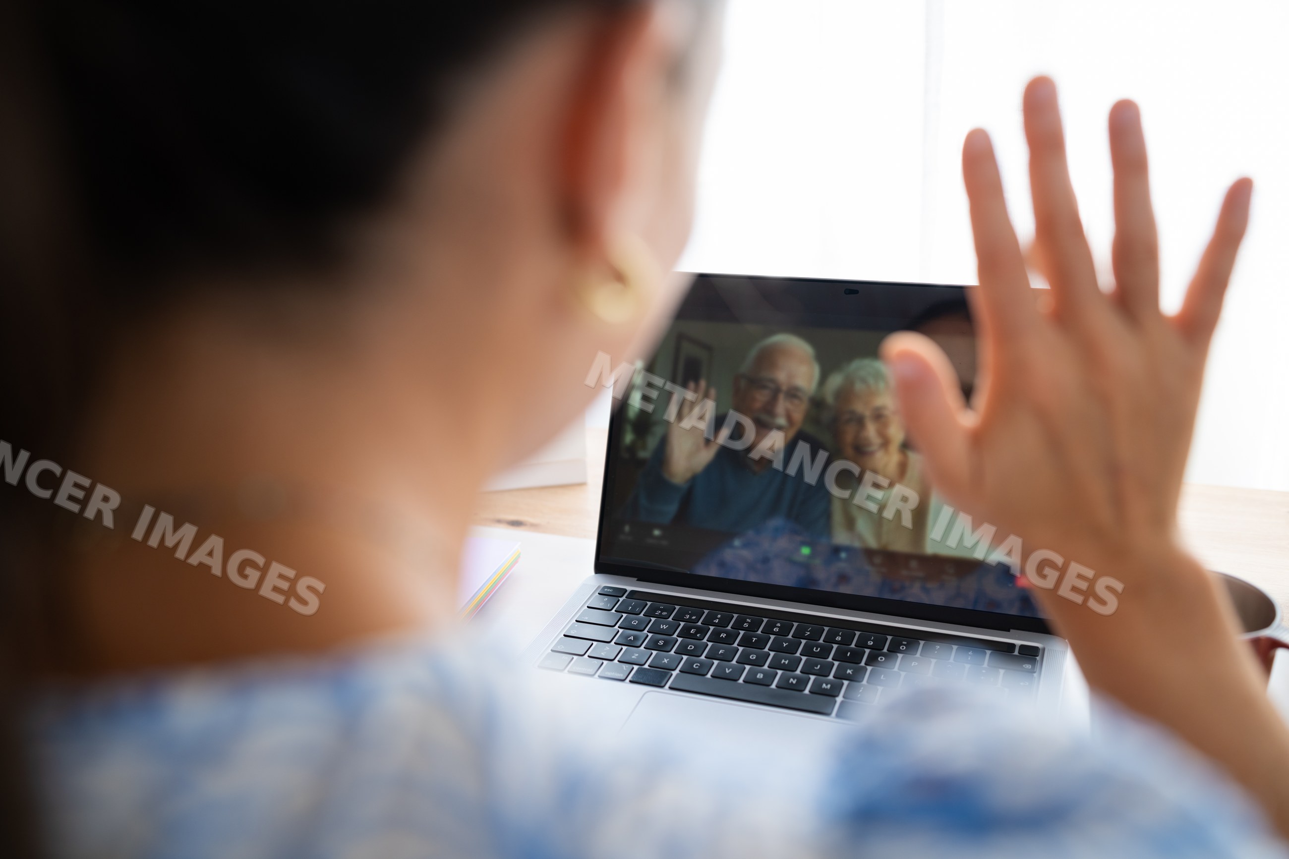Elderly couple waving during video call on laptop at home office