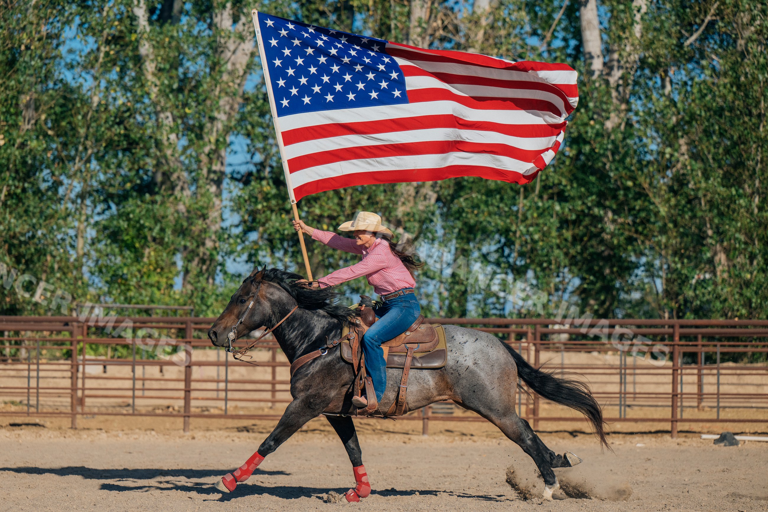 White woman riding horse carrying american flag in rodeo arena