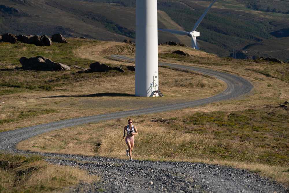 A white woman runs on a gravel trail by wind turbines in Galicia Spain