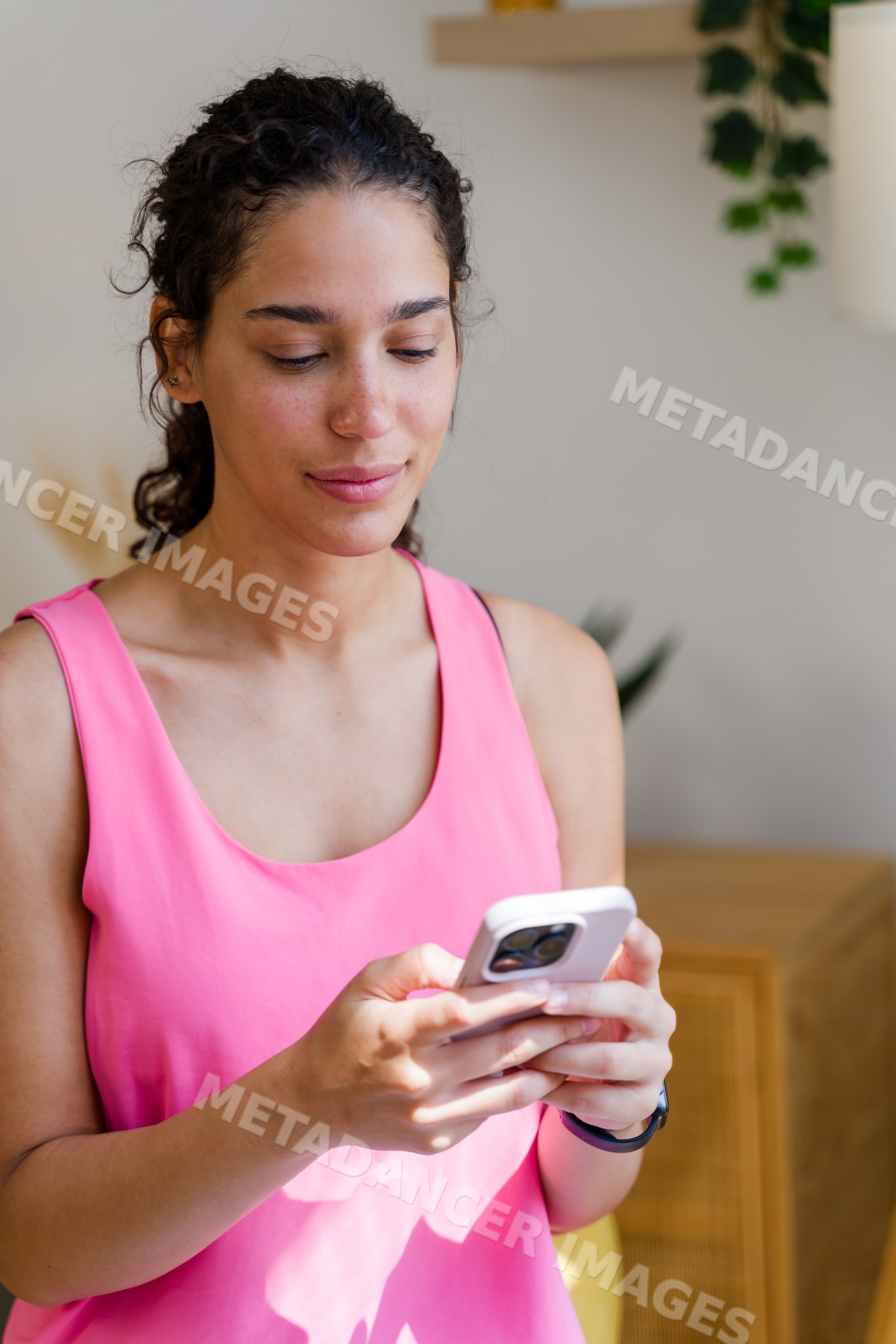 A young Hispanic woman uses her smartphone indoors in a home