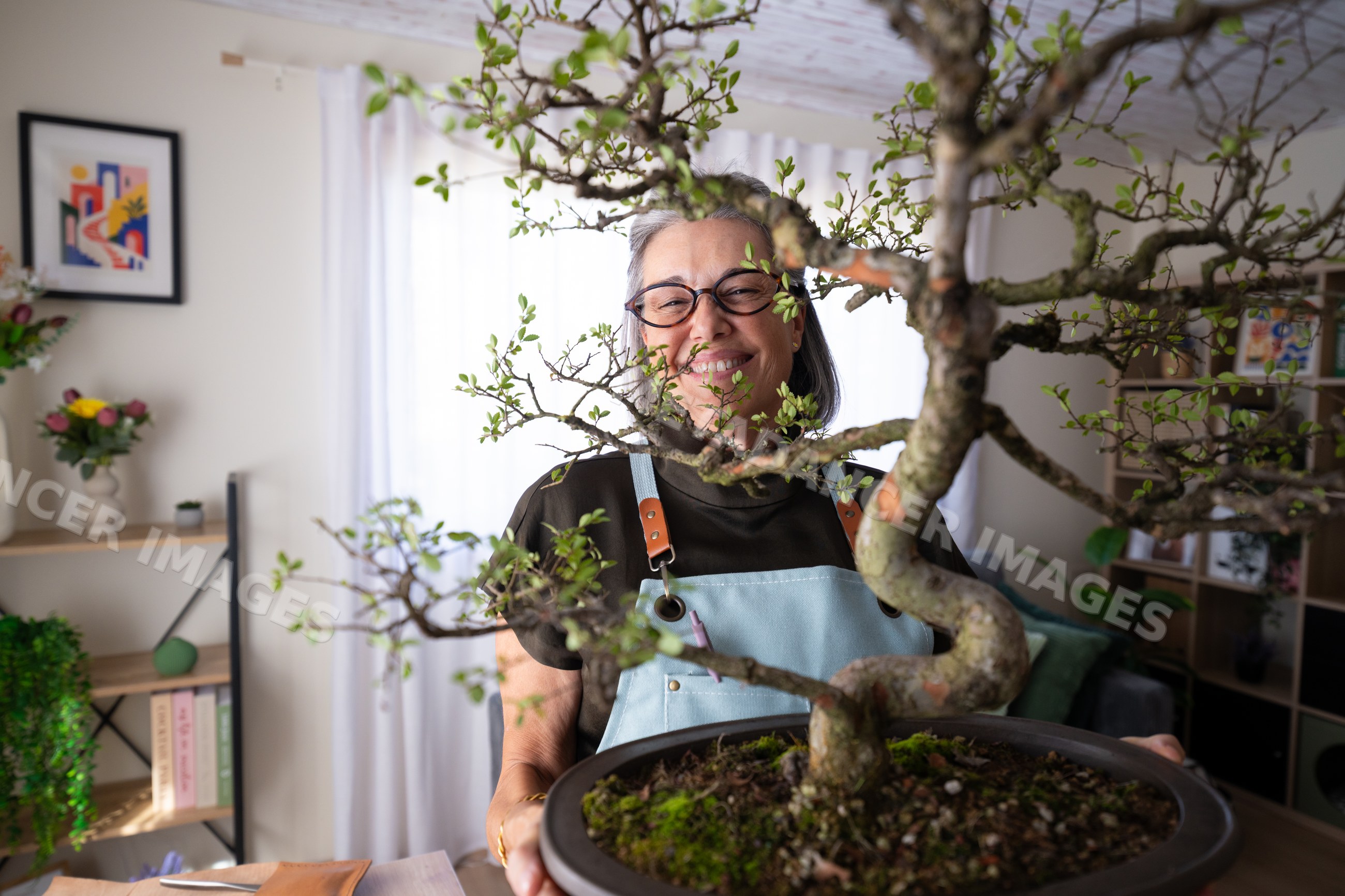 White woman holding a bonsai tree indoors in a cozy home environment