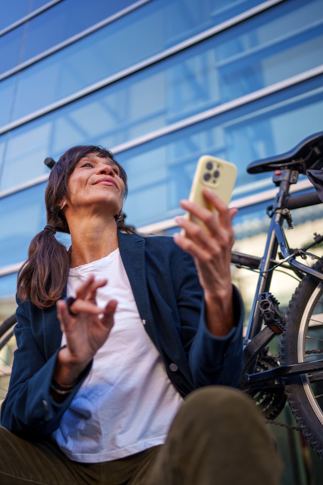 Hispanic woman using smartphone near bicycle outside modern building