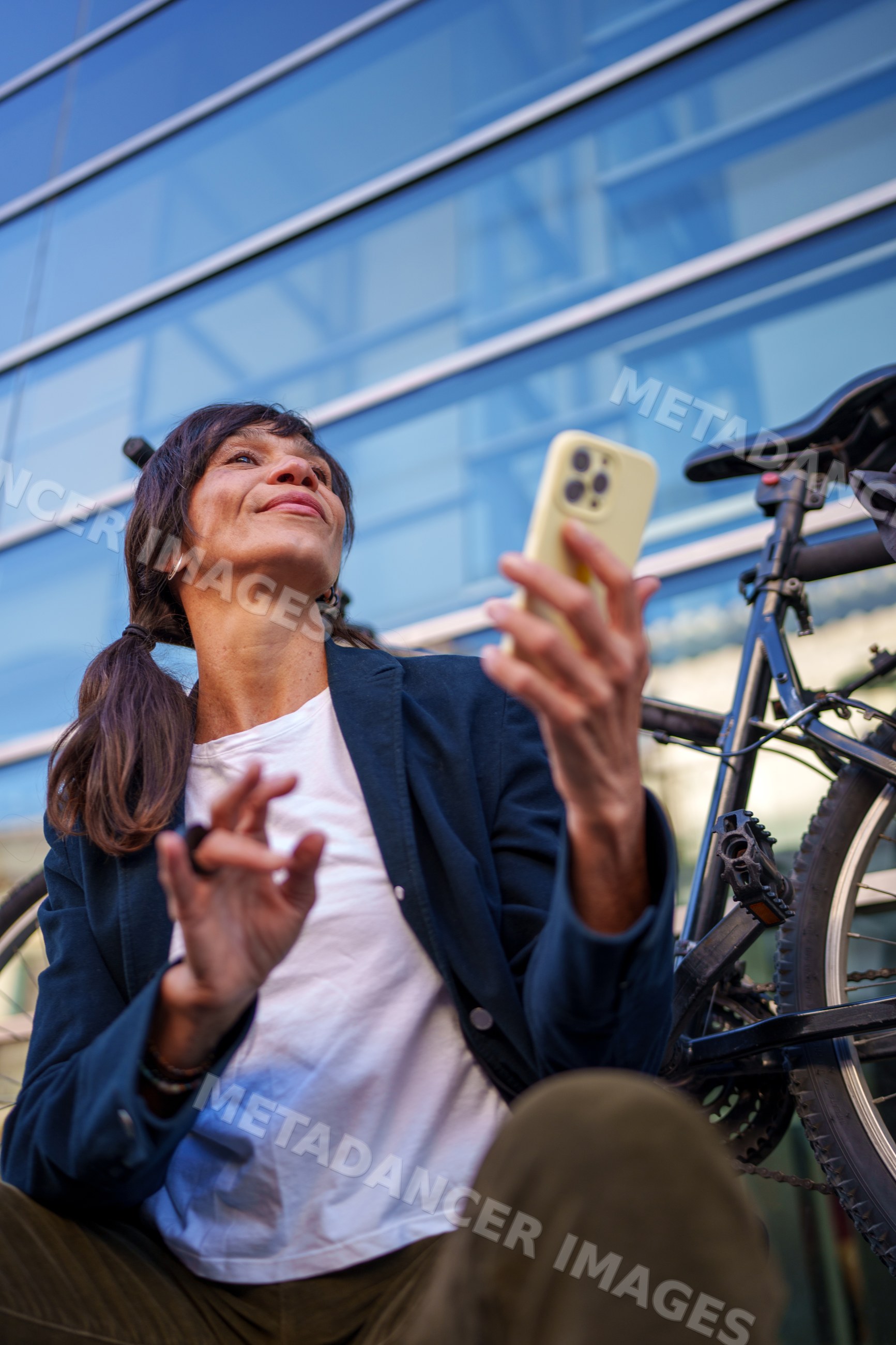 Hispanic woman using smartphone near bicycle outside modern building
