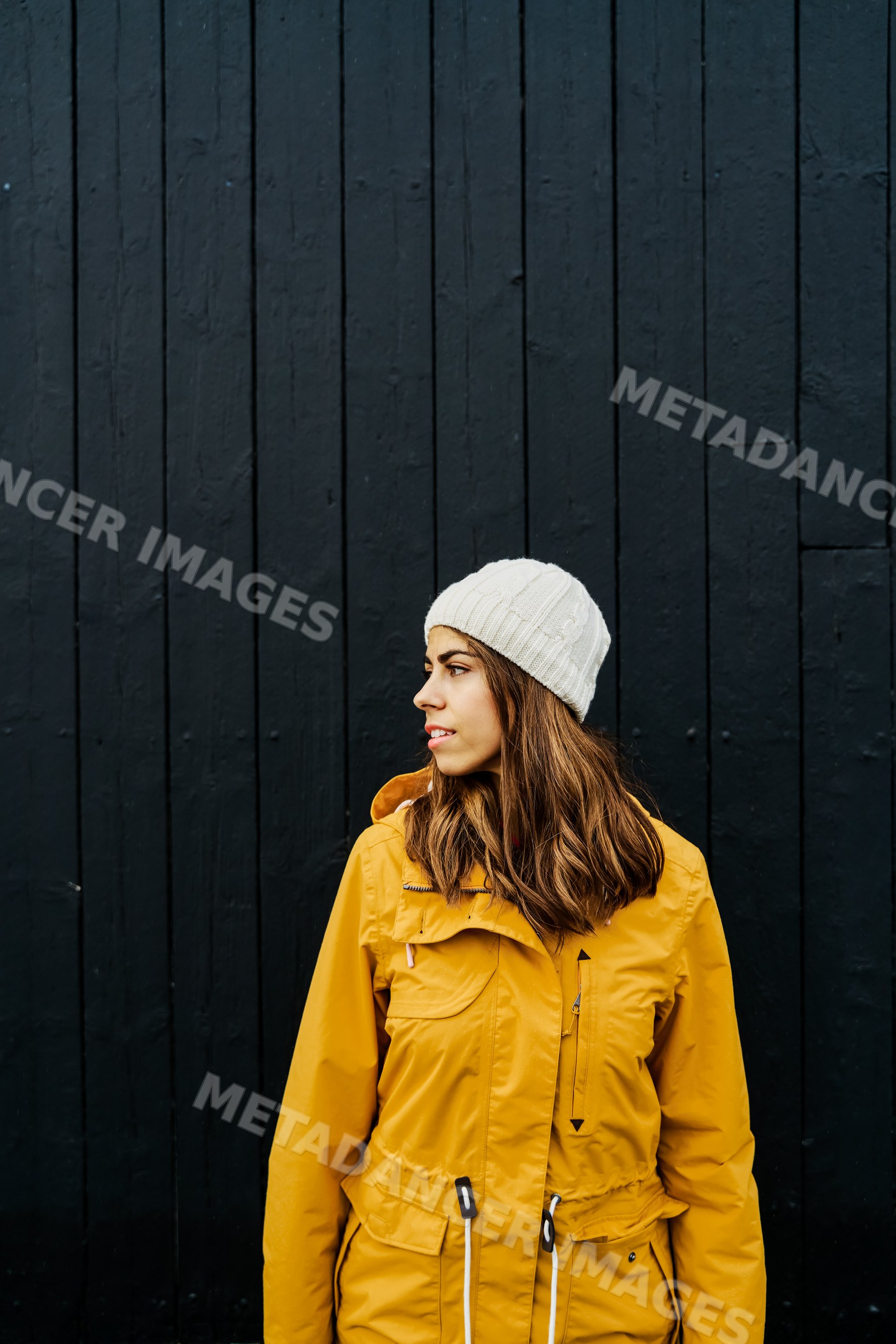 A young white woman in yellow jacket looking sideways by a black