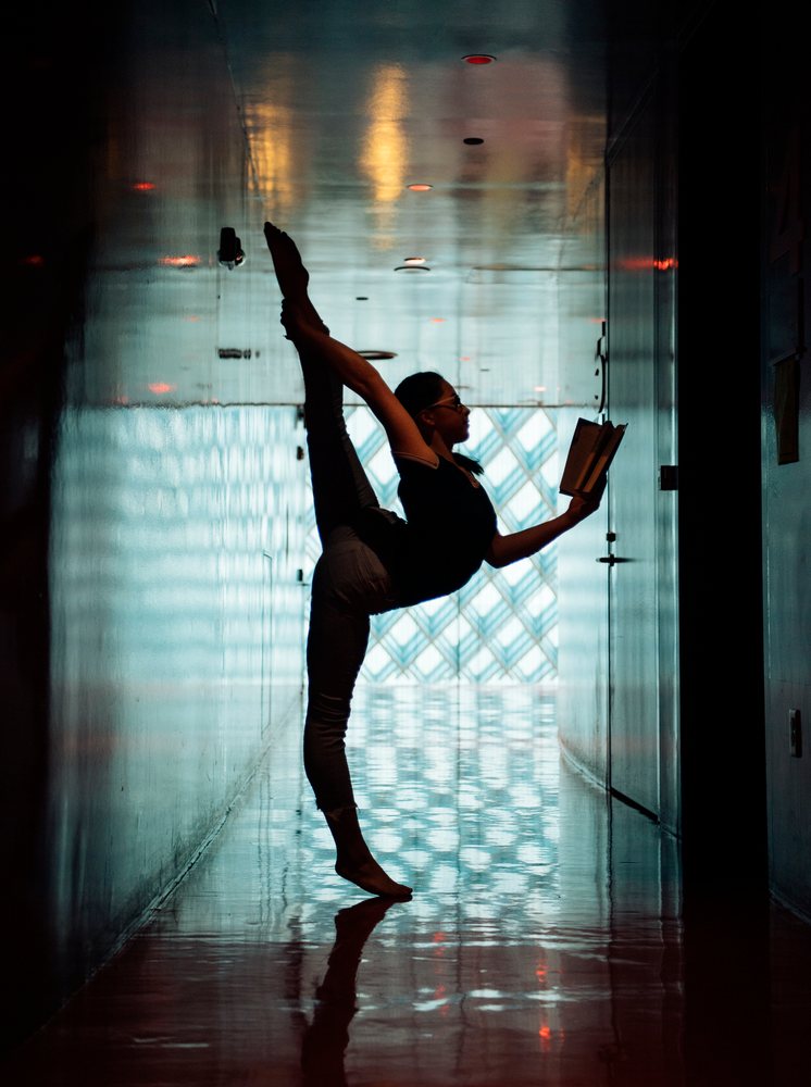 A girl stretches in a yoga pose while reading a book in a library