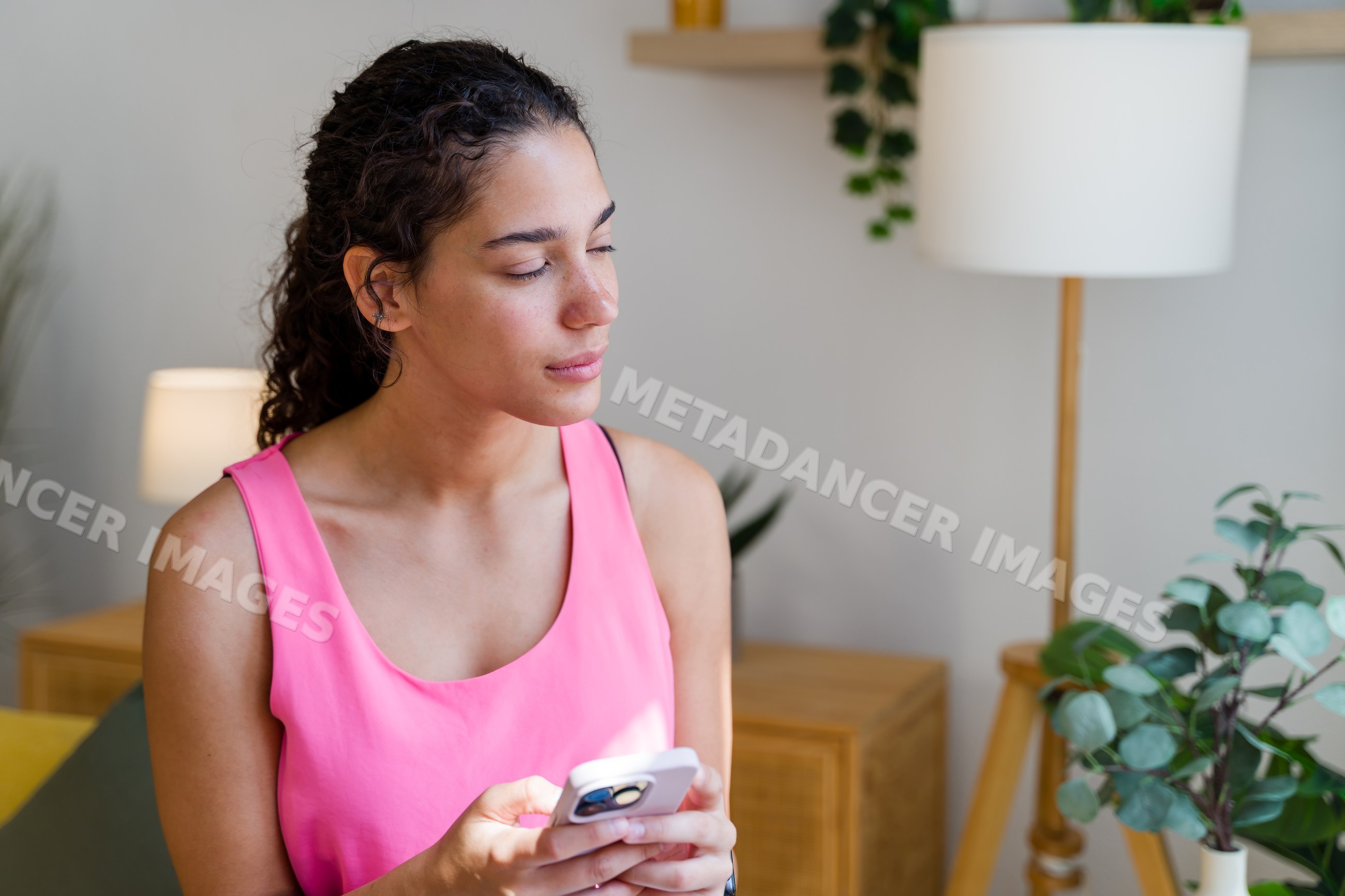 Hispanic Woman in a pink top using a mobile phone indoors in a home