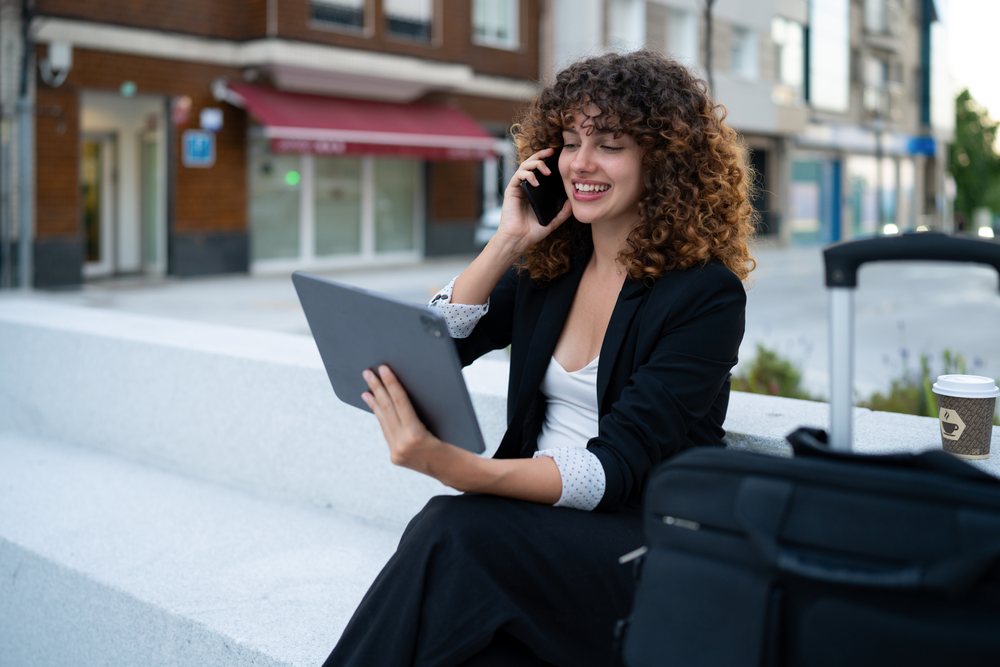 Business white woman using tablet and phone while waiting outdoors