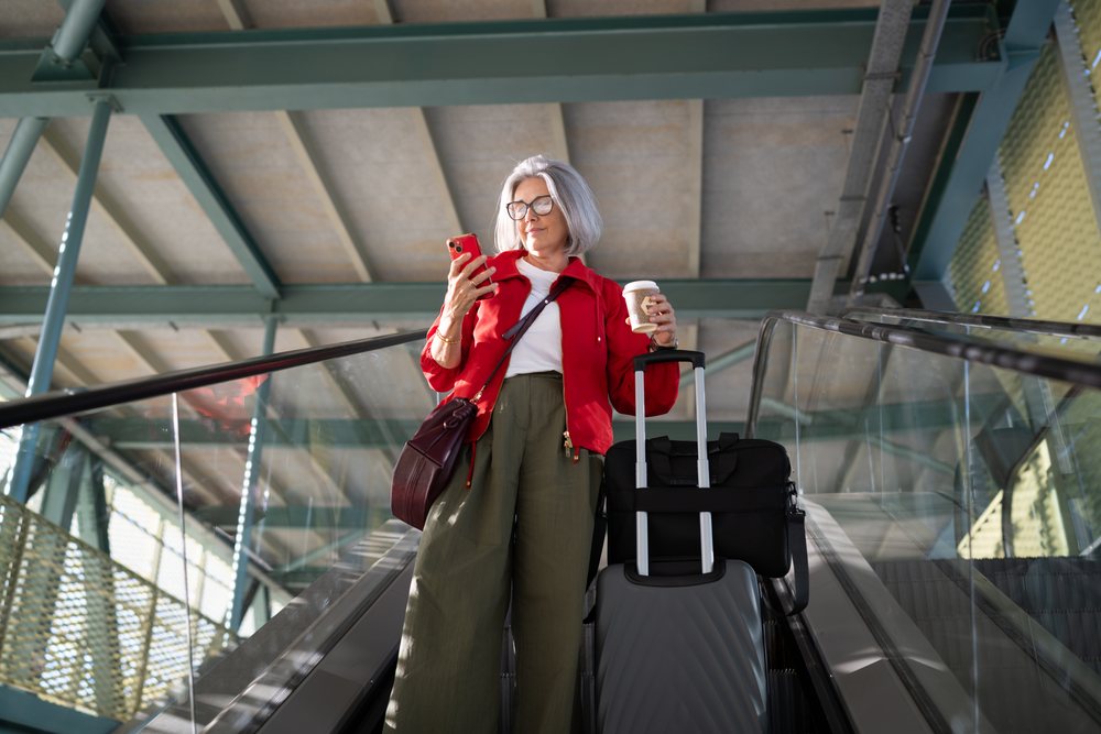 White woman on escalator holding coffee and using smartphone