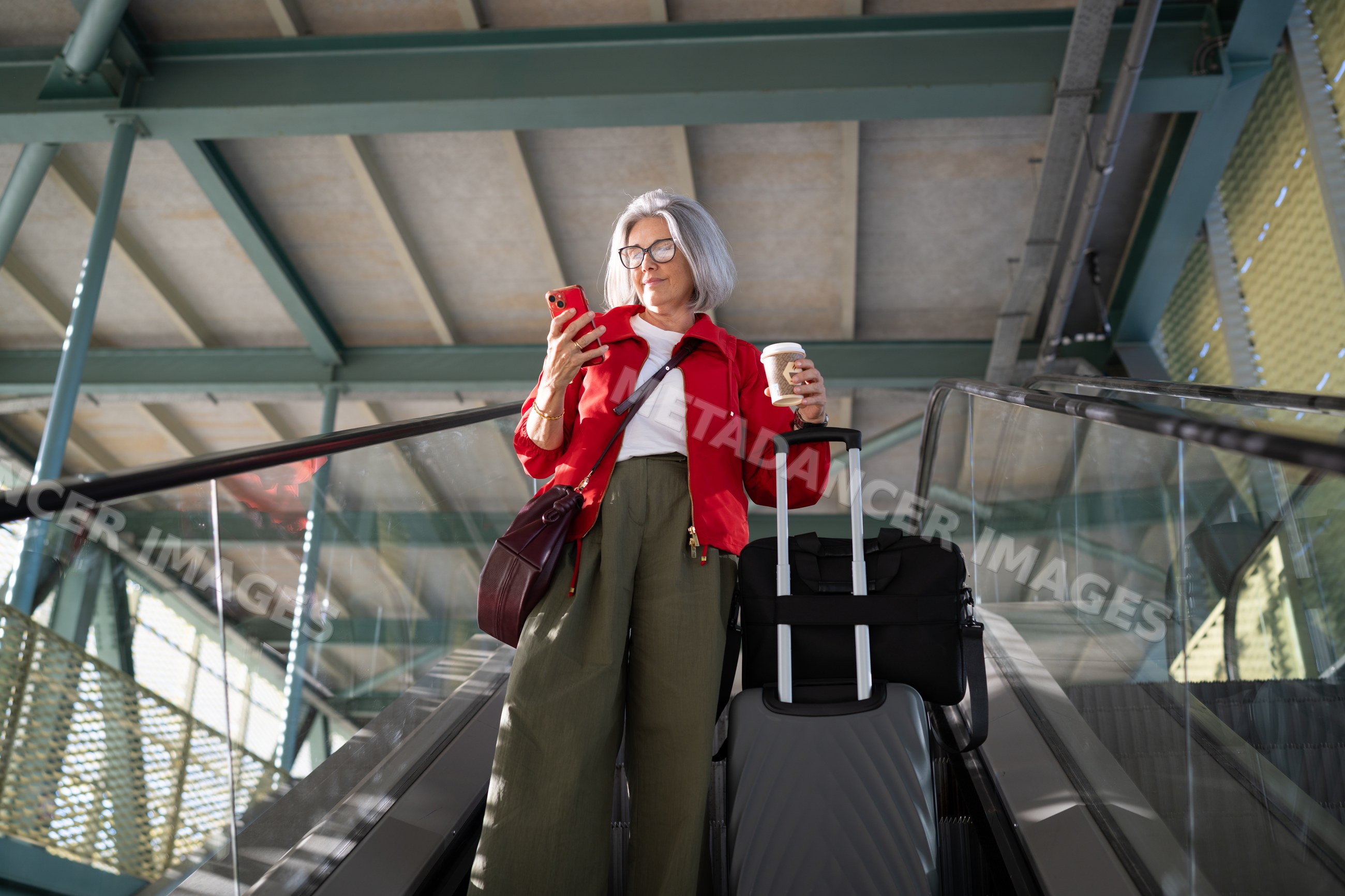 White woman on escalator holding coffee and using smartphone
