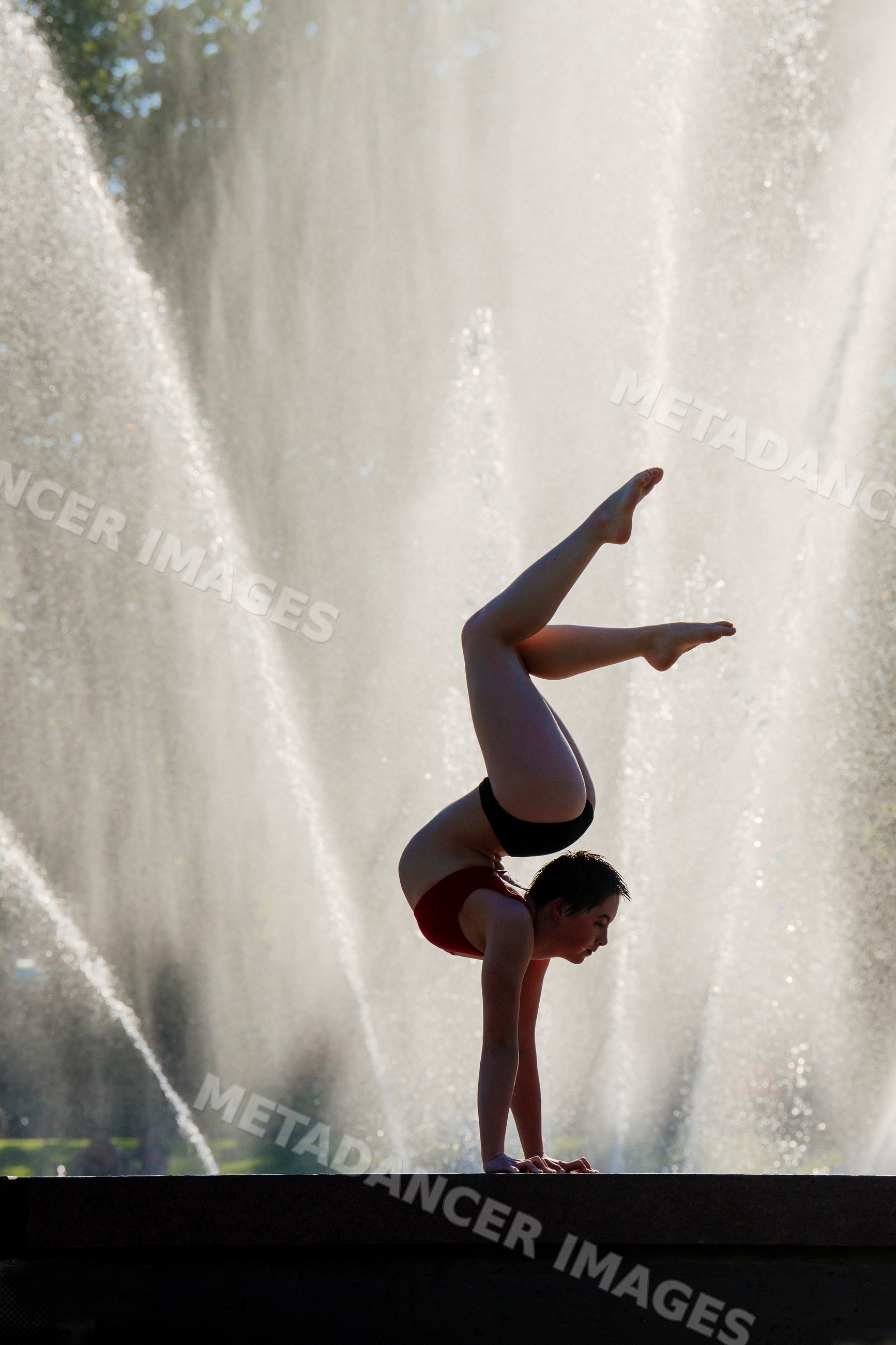 White woman performing handstand yoga pose by water fountain outdoors